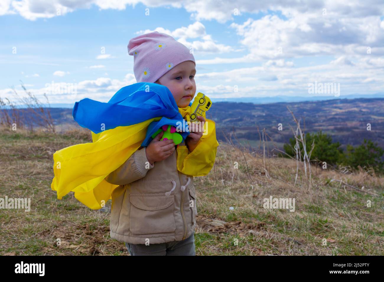 Una bambina con una bandiera dell'Ucraina contro le colline e la natura Ucraina e cielo nuvoloso blu. Ritratto di una bambina patriottica con la bandiera di Ukra Foto Stock