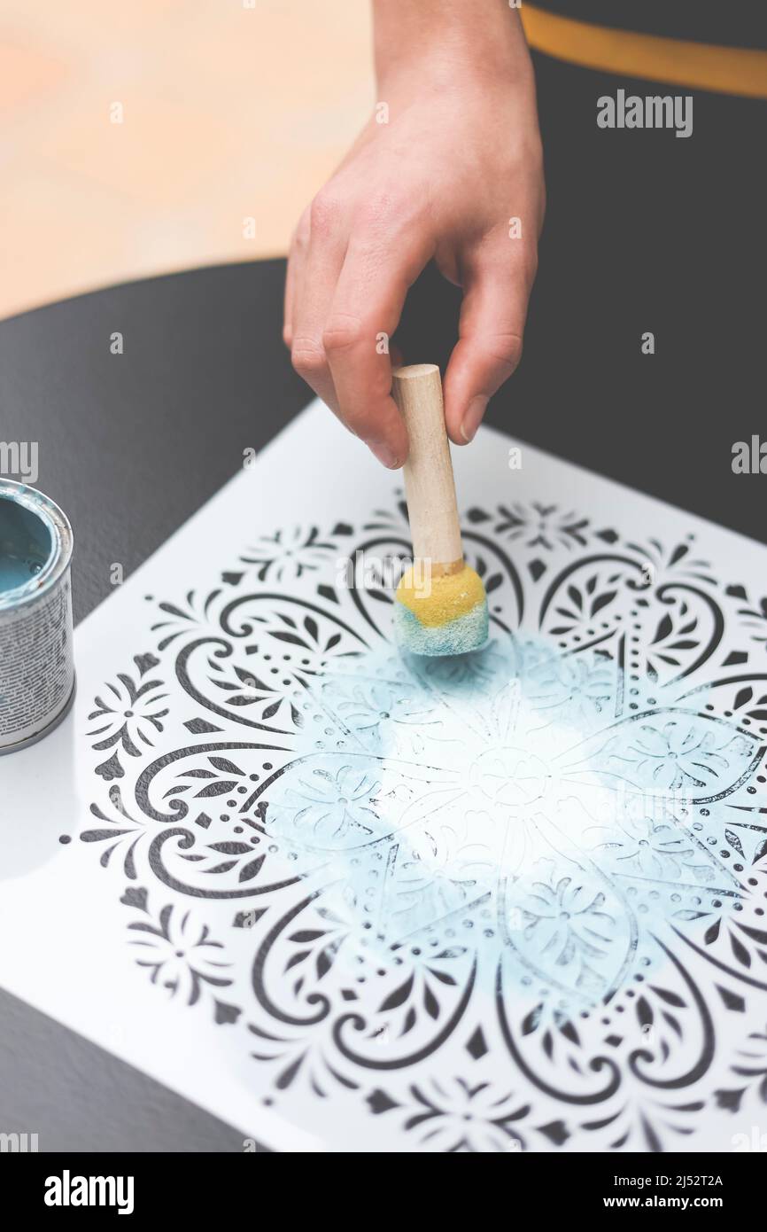 Persona che usa un dabber con vernice acrilica su uno stencil di mandala Foto Stock