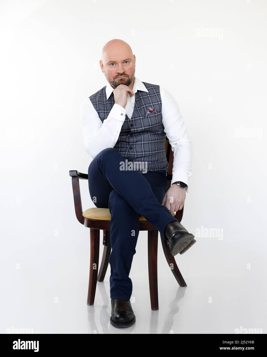 Ritratto di pensieroso uomo d'affari di mezza età in gilet grigio, jeans blu, camicia bianca seduta, testa sul mento. Foto Stock
