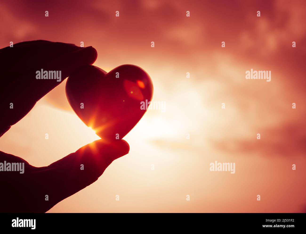 Mano che tiene il cuore sullo sfondo del cielo del tramonto. Amore e San Valentino sfondo giorno. Foto Stock