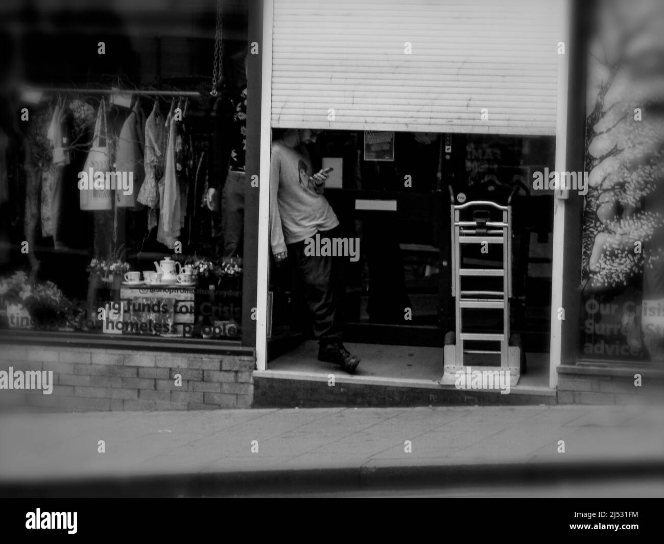 Incongruo trovato ancora vita di persona, senza volto, in piedi dietro un mezzo chiuso negozio otturatore con scala e scaffale di vestiti Foto Stock