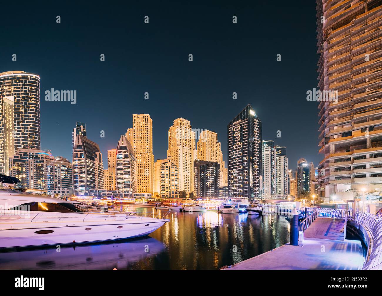 Jetty con molti yacht ormeggiati nelle illuminazioni notturne. Vista notturna dello skyline di Dubai Marina Foto Stock