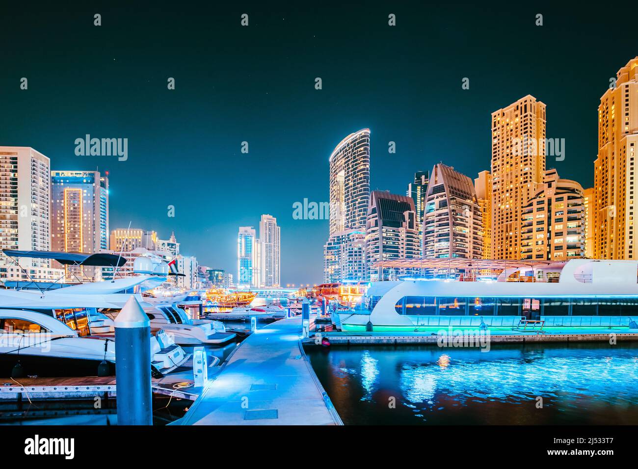 Vista notturna di Dubai Marina Towers and Boats, barche ormeggiate vicino al molo nelle illuminazioni notturne Foto Stock