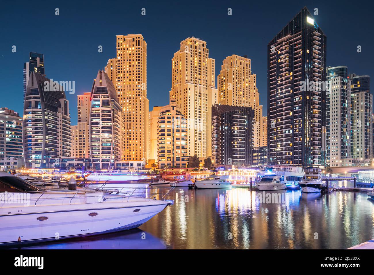 Jetty con molti yacht ormeggiati nelle illuminazioni notturne. Vista notturna delle Dubai Marina Towers Foto Stock