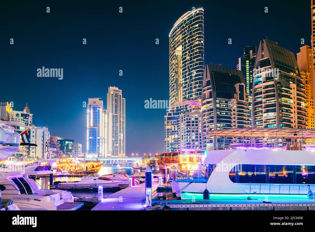 Vista notturna del grattacielo a Dubai Marina e Boats, barche ormeggiate vicino al molo nelle illuminazioni notturne Foto Stock