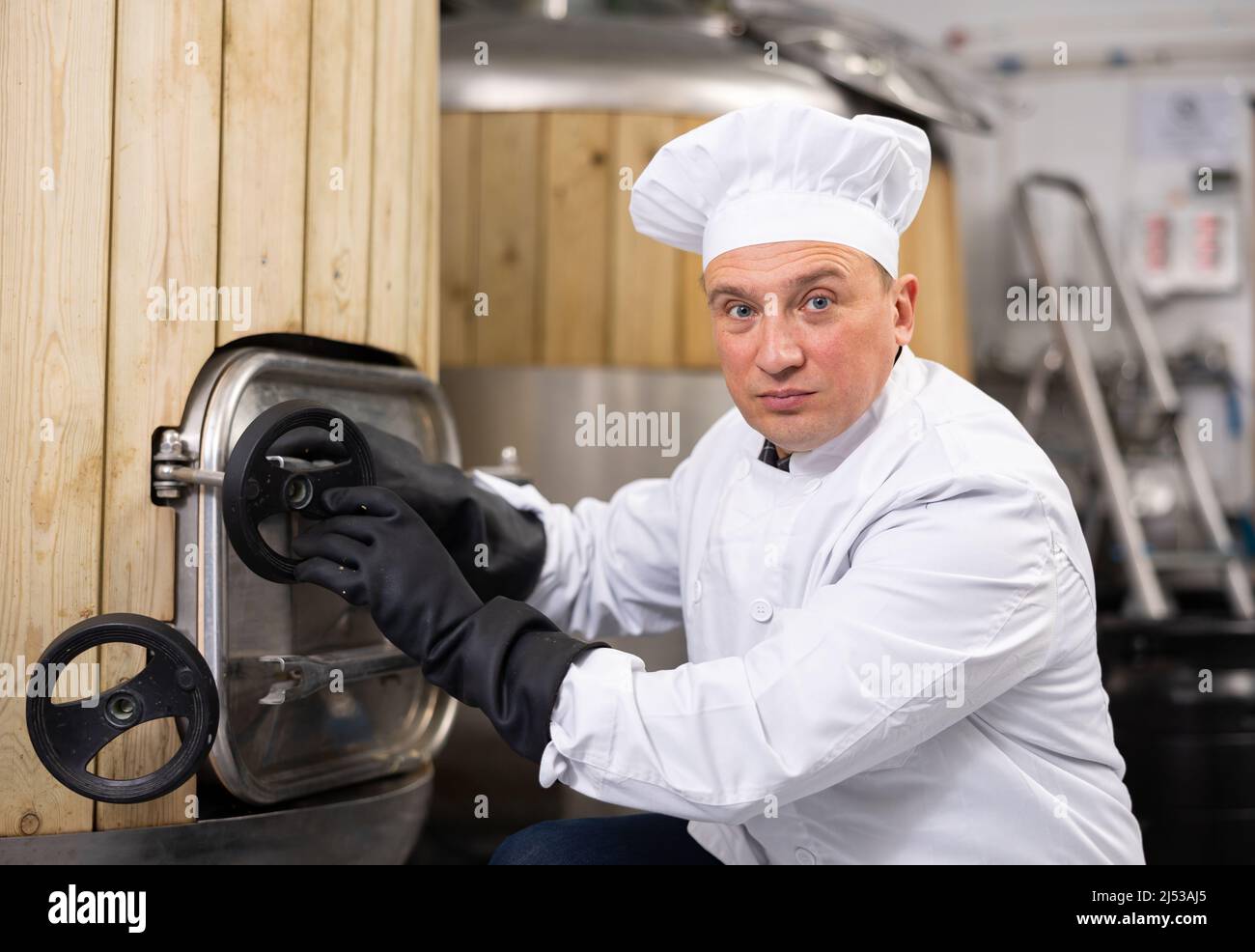 Il proprietario del birrificio si occupa del controllo del serbatoio di fermentazione in officina Foto Stock