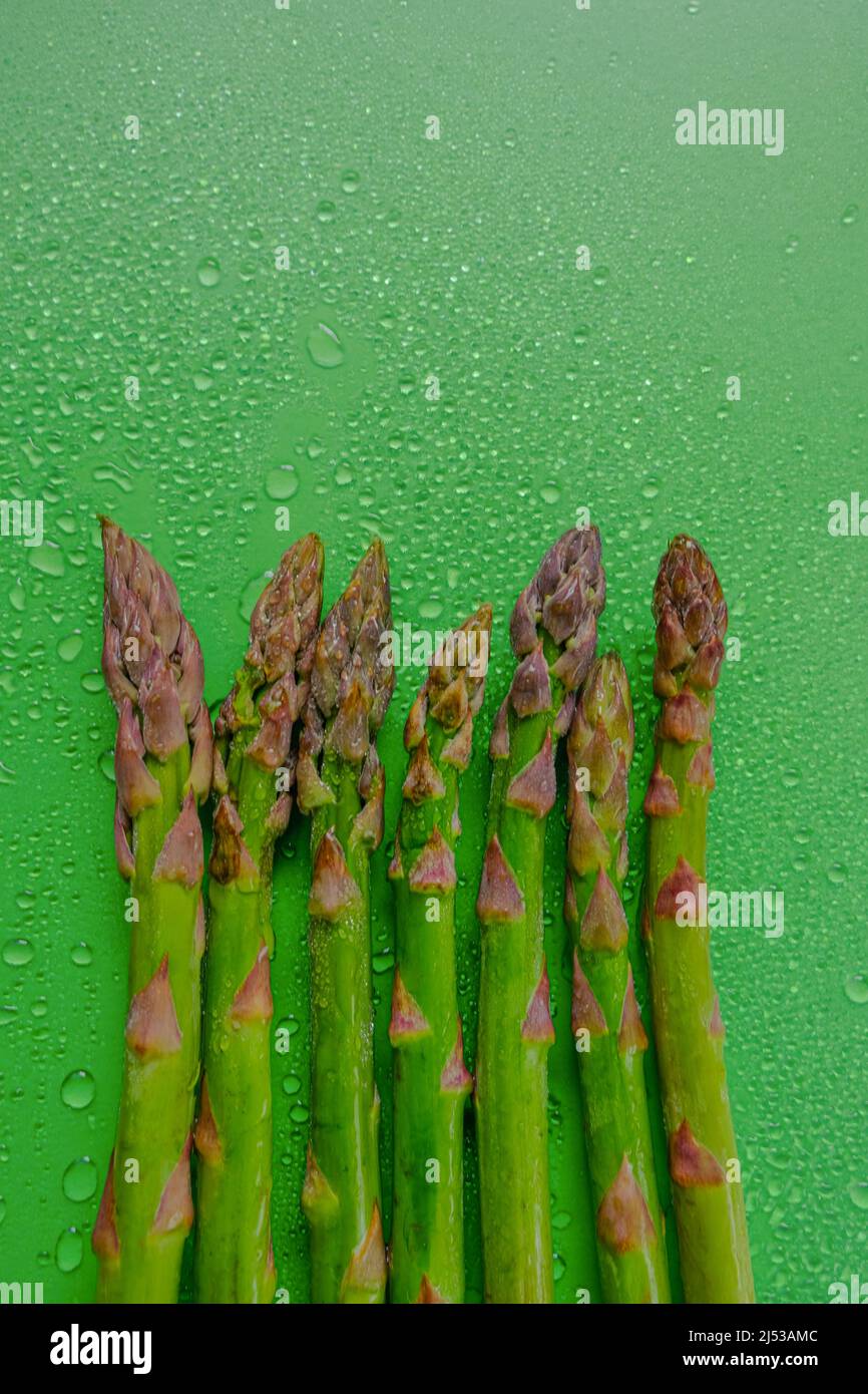 Asparagi riga verde in acqua gocce su sfondo verde. Raccolta di asparagi verdi.Spring Farm bio verdure fresche Foto Stock