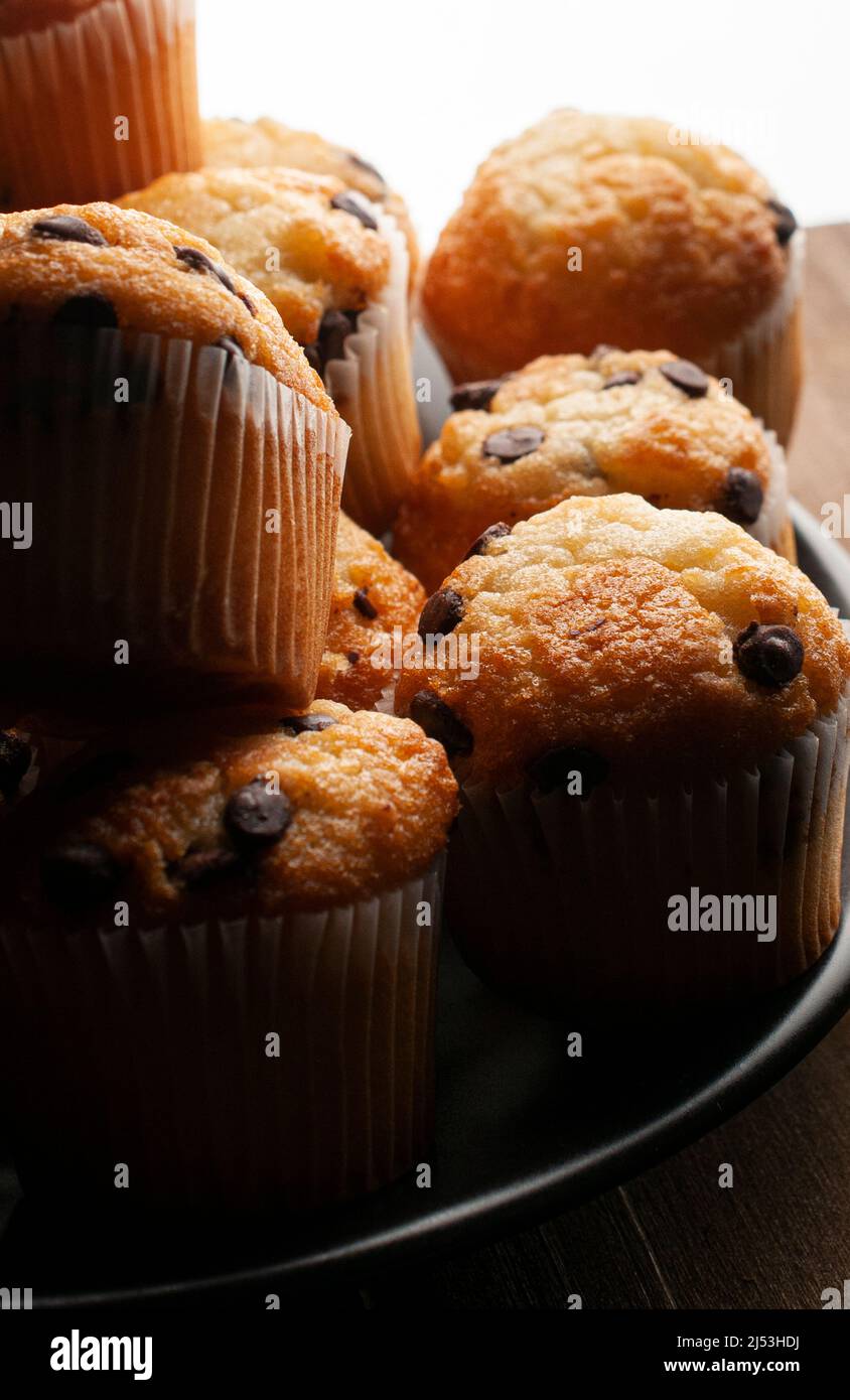 Macro fotografia chiaroscuro o dark food, cupcake alla vaniglia con gocce di cioccolato su un piatto nero, concetto di cibo fatto in casa Foto Stock