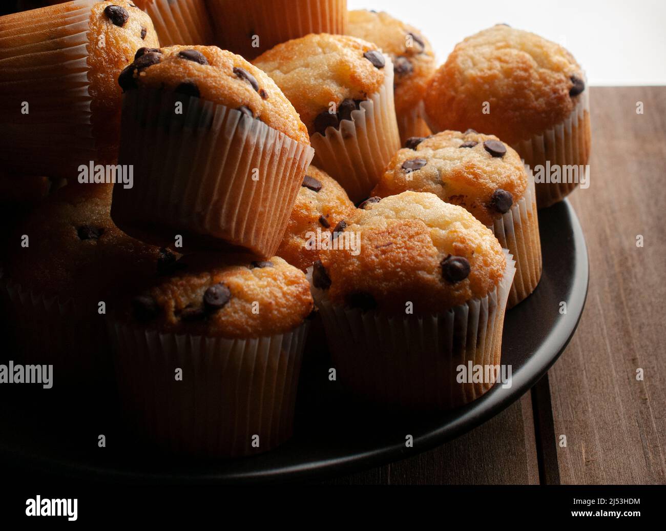 Macro fotografia chiaroscuro o dark food, cupcake alla vaniglia con gocce di cioccolato su un piatto nero, concetto di cibo fatto in casa Foto Stock