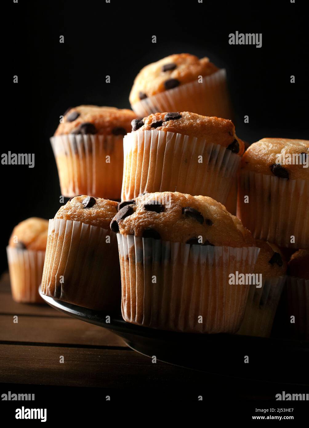 Macro fotografia chiaroscuro o dark food, cupcake alla vaniglia con gocce di cioccolato su un piatto nero, concetto di cibo fatto in casa Foto Stock