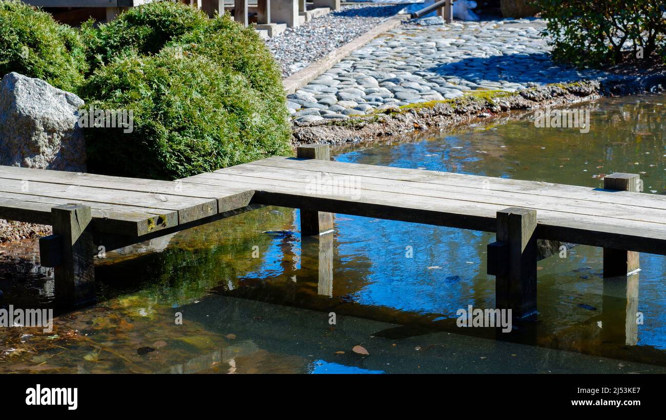 Ponte di legno su un piccolo ruscello in un giardino giapponese. La strada è lastricata di pietre e ciottoli. Solo materiali naturali. Bellissima acqua lan Foto Stock