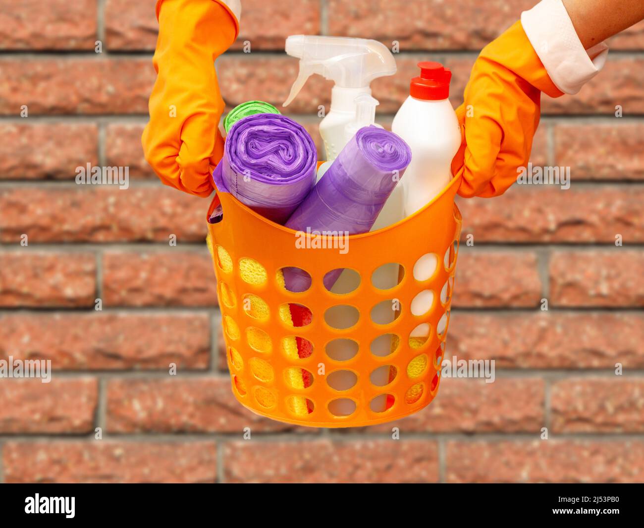 Le mani della donna in guanto protettivo con sacchetti per rifiuti, bottiglie di detergente per vetri in cestino arancione. Foto Stock