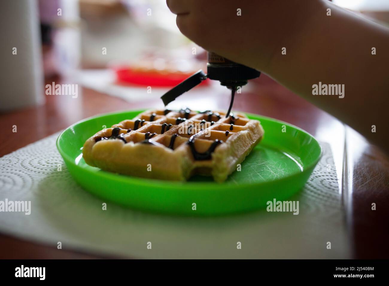 I bambini versano lo sciroppo di cioccolato su un waffle. Primo piano Foto Stock