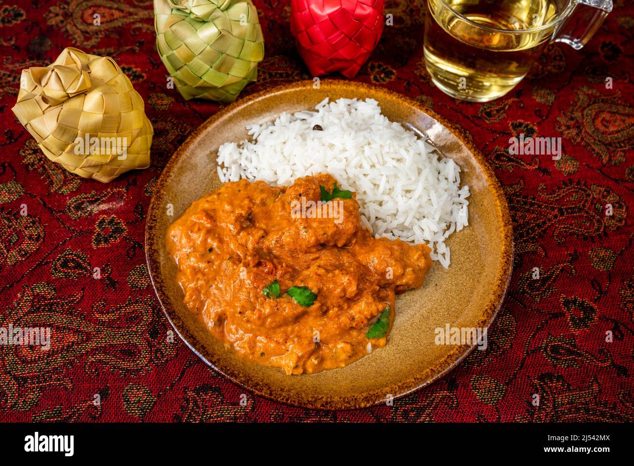 Pollo tikka masala con riso sul piatto, 3 scatola di bambù spezia, tazza di tè su un panno rosso da tavolo. Pranzo o cena indiana, primo piano. Foto Stock