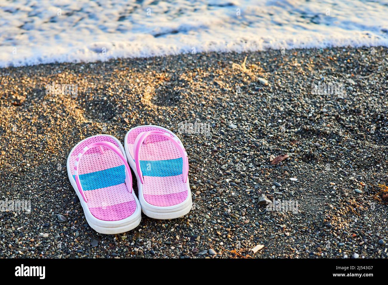 Pantofole rosa per bambini su una spiaggia di ciottoli Foto Stock