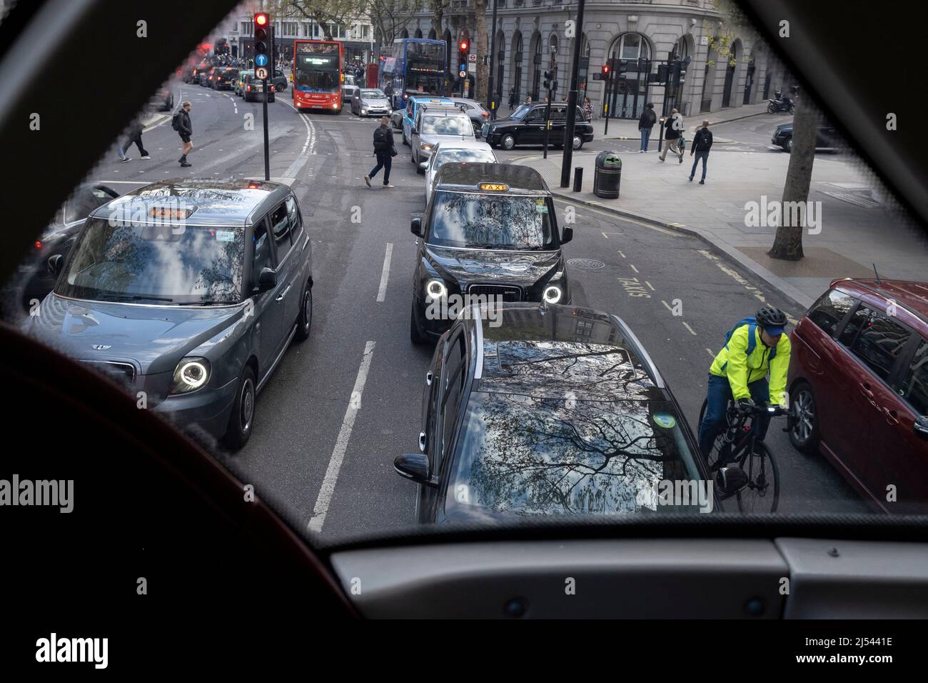 I pedoni attraversano la strada e un ciclista passa auto e taxi che si estendono in lontananza, visto dal ponte superiore di un autobus di Londra ad Aldwych, il 13th aprile 2022, a Londra, Inghilterra. Foto Stock