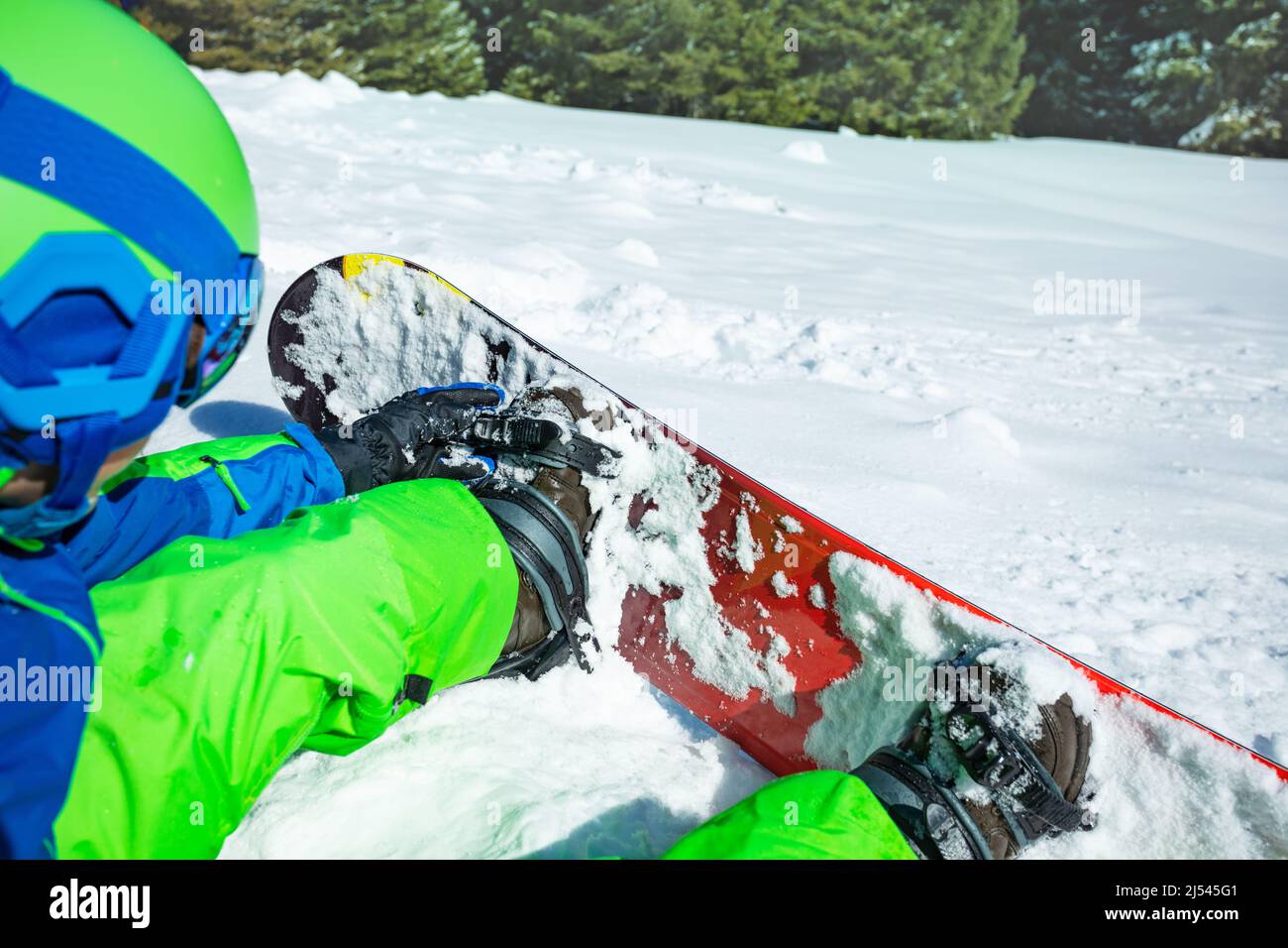 Primo piano del ragazzo che fissa lo snowboard seduto nella neve Foto Stock