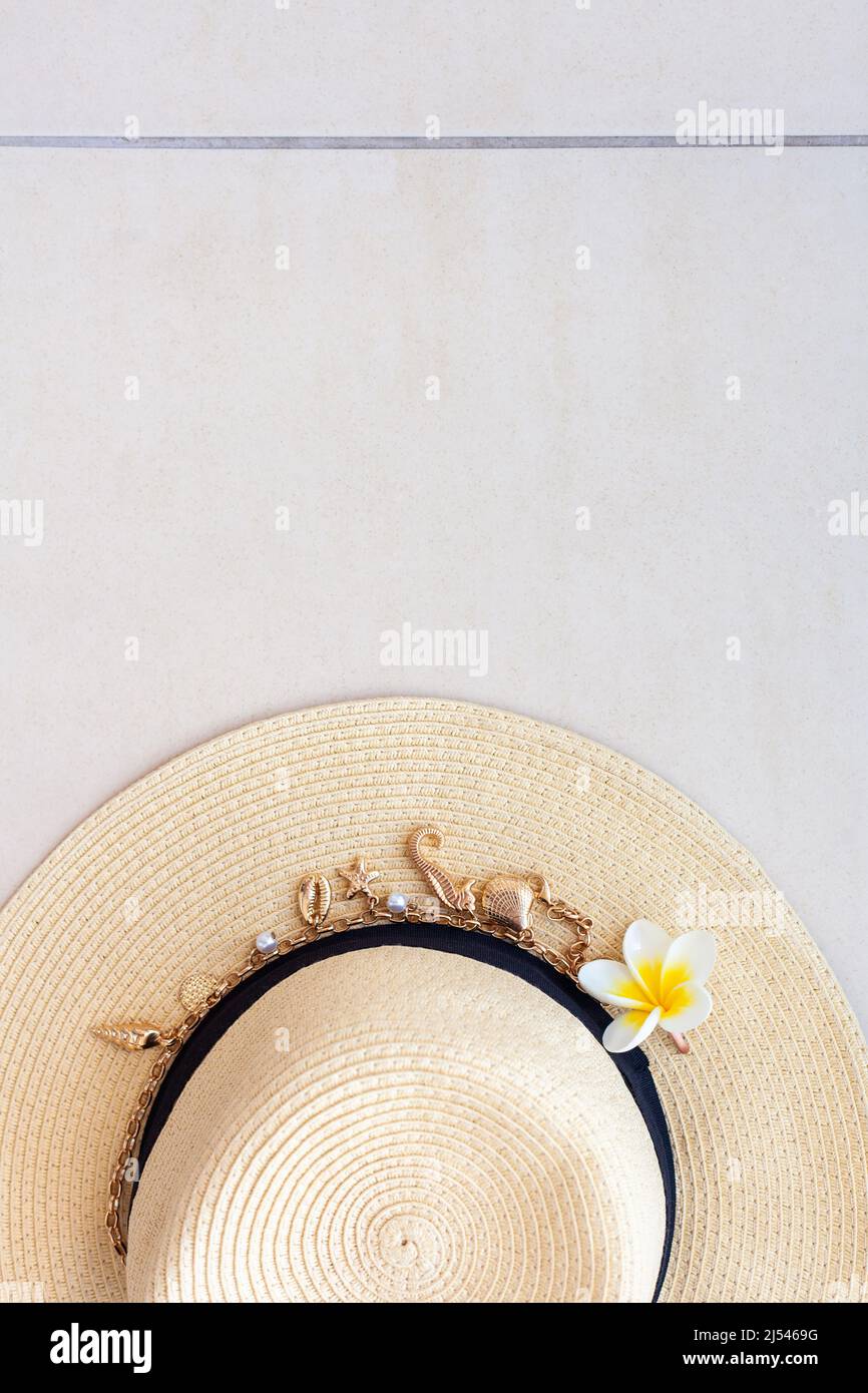 Cappello estivo di paglia con collana con conchiglie e perle e il fiore della piumeria sul pavimento piastrellato, vista dall'alto. Il concetto di vacanza estiva e. Foto Stock
