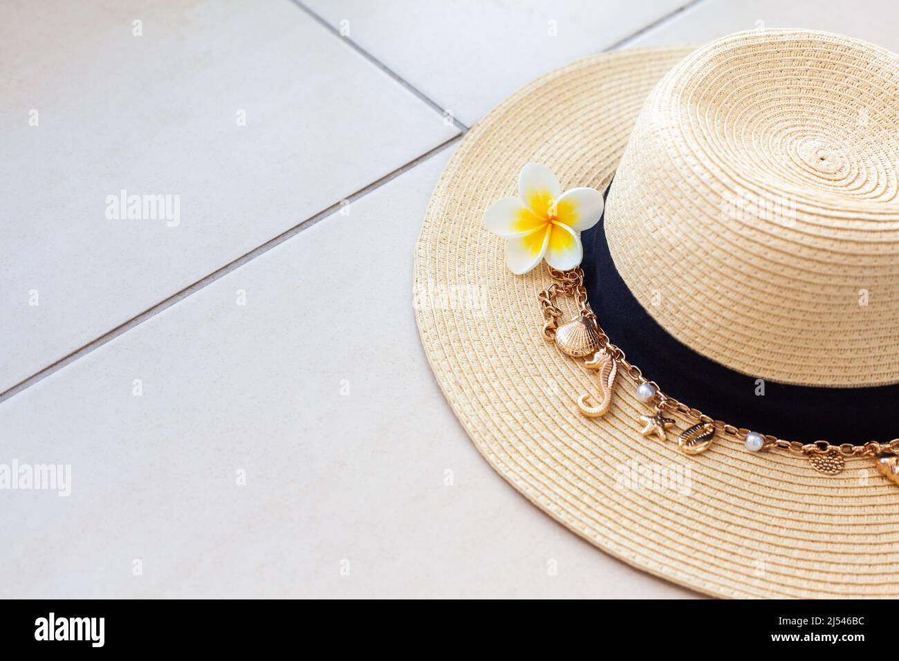 Cappello estivo di paglia con collana con conchiglie e perle e fiore di piumeria sul pavimento piastrellato con spazio copia. Il concetto di vacanze estive Foto Stock
