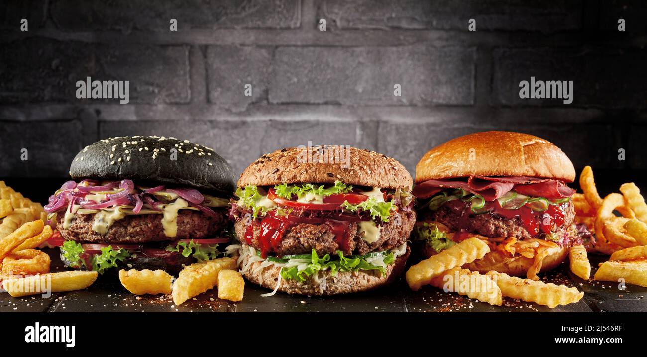 Appetitosi vari hamburger e patatine fritte poste in fila sul tavolo su sfondo scuro Foto Stock