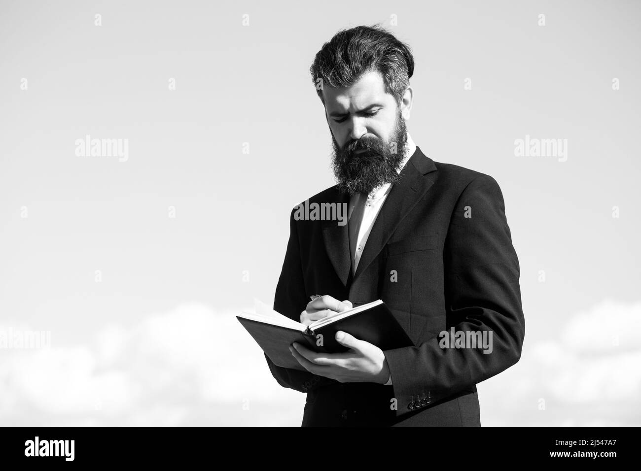 Uomo d'affari con cielo. Ritratto con spazio di copia di uomo serio che tiene il copybook e con penna con espressione premurosa su sfondo cielo. Foto Stock