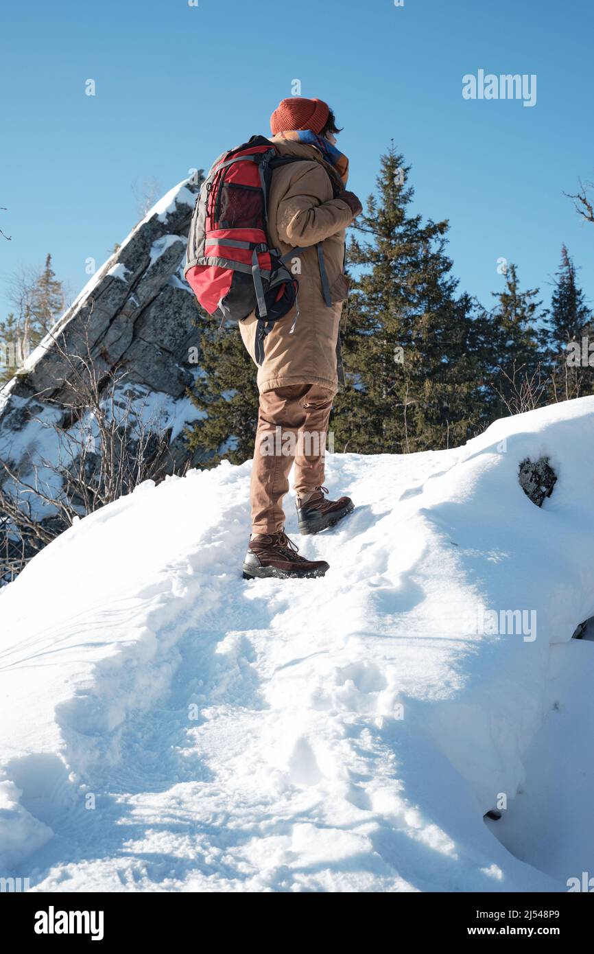 Scatto verticale ad angolo basso del giovane uomo che indossa abiti caldi e zaino che si fa un'escursione fino alla cima della montagna Foto Stock