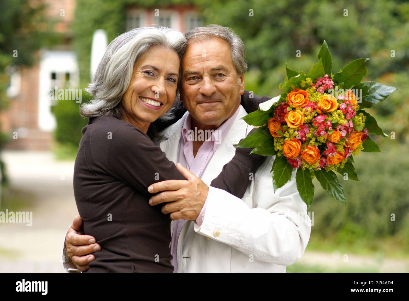 coppia anziana nel parco, l'uomo la abbraccia amorevolmente dopo averle consegnato un bouquet di fiori Foto Stock