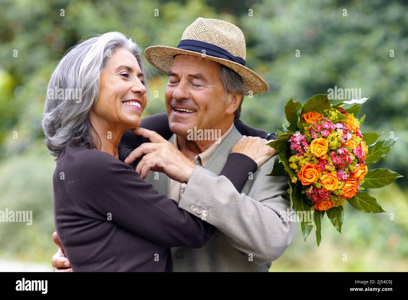 coppia anziana nel parco, l'uomo la abbraccia amorevolmente dopo averle consegnato un bouquet di fiori Foto Stock