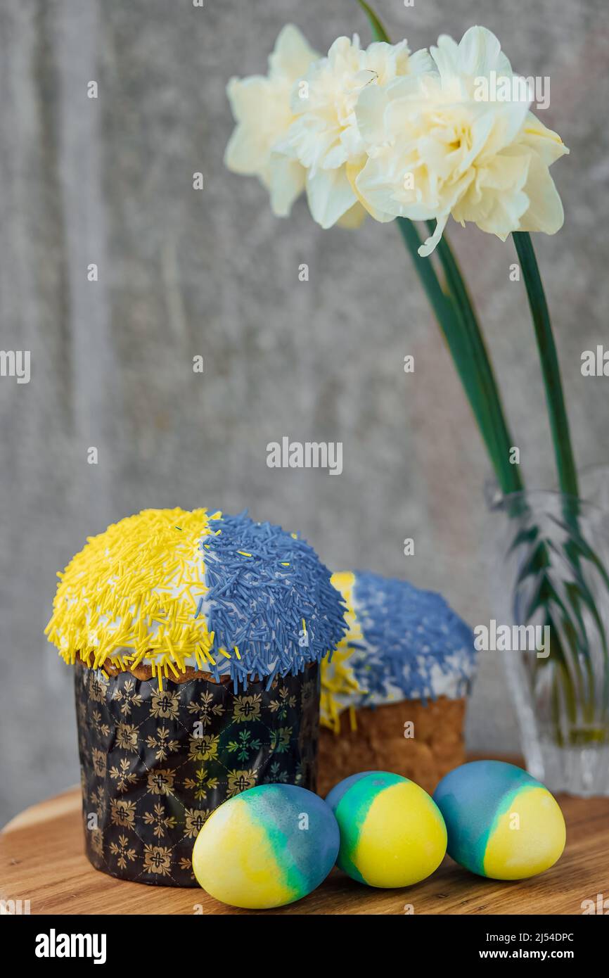 Dolci di Pasqua deliziosi nei colori della bandiera dell'Ucraina, uova di Pasqua di colore giallo-blu su un tavolo di legno con fiori sullo sfondo. Luogo f Foto Stock