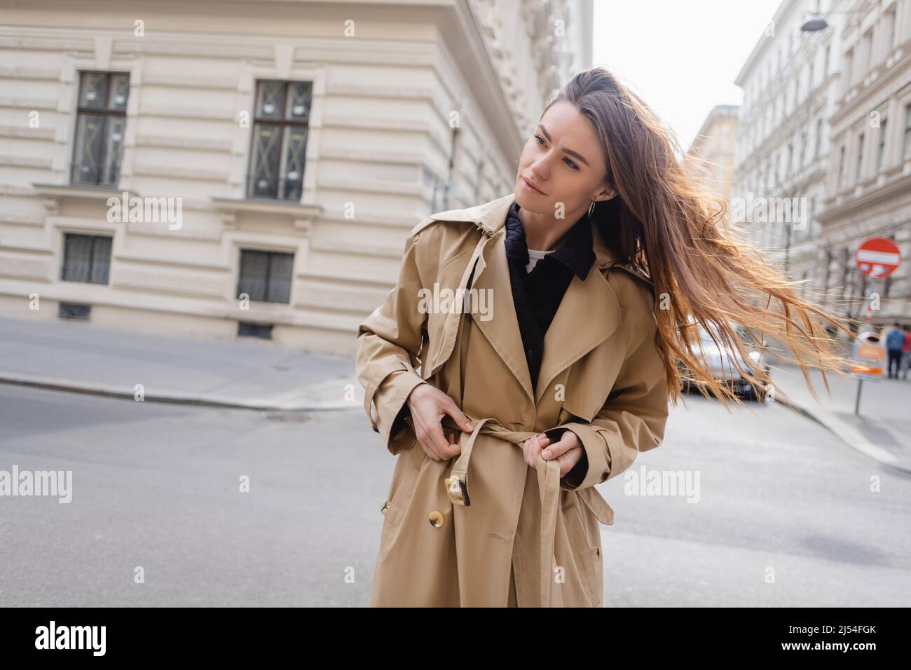 graziosa giovane donna che regola la cintura su trench beige Foto Stock