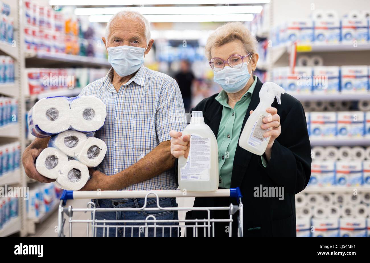 coppia matura indossando maschera e guanti con protezione covid sceglie asciugamani di carta nel reparto di supermercato Foto Stock
