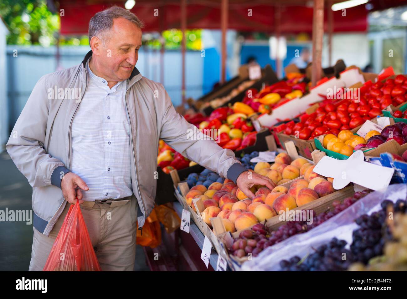 Uomo che sceglie le pesche nel mercato Foto Stock