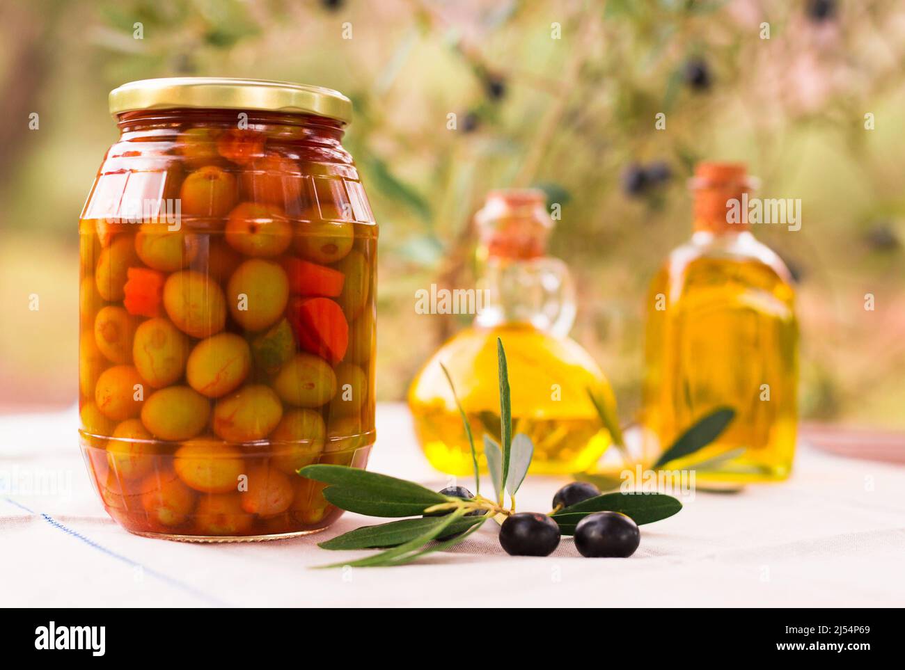 vasetto di vetro di olive in aceto, olio e olive su tavola in un campo d'oliva Foto Stock