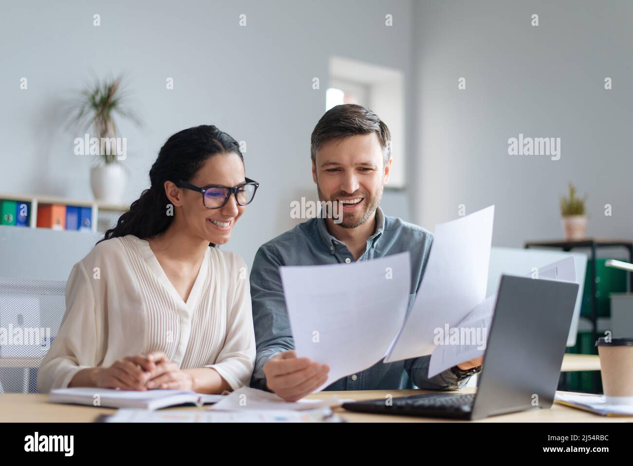 Allegri dipendenti aziendali maschili e femminili che guardano attraverso documenti, collaborano, usano il laptop in un ufficio moderno Foto Stock