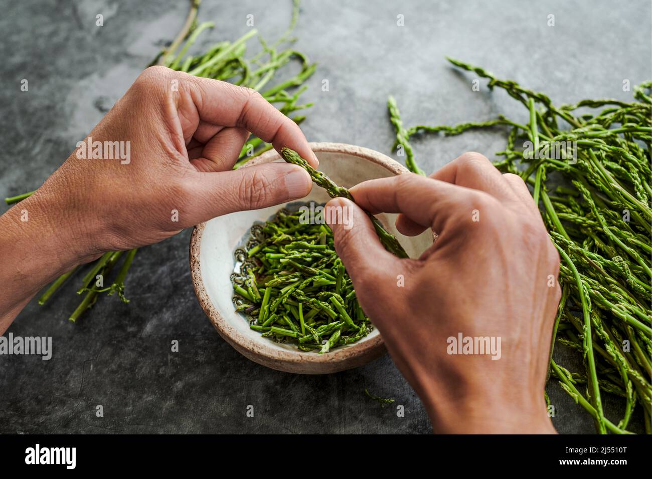 un giovane taglia la parte commestibile di alcuni asparagi selvatici, su una superficie di pietra accanto ad un mazzetto di asparagi selvatici Foto Stock