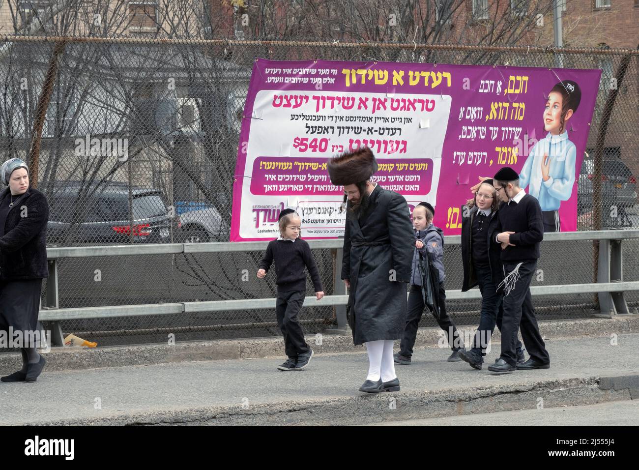 Una famiglia ebrea ortodossa cammina su Lee Ave sulla Pasqua. Dietro di loro è un segno per un matchmaker che si paga solo se riescono. A Brooklyn, New York. Foto Stock