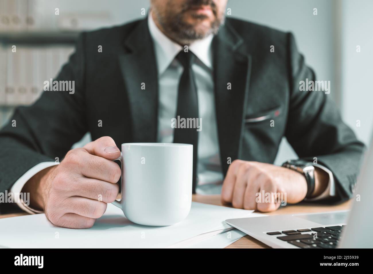 Il lavoratore di ufficio del collare bianco tiene una tazza di caffè alla sua scrivania, fuoco selettivo Foto Stock