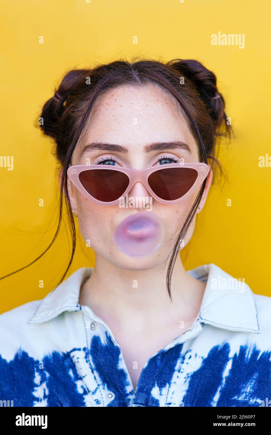 donna che soffia una bolla di gomma su uno sfondo giallo Foto Stock