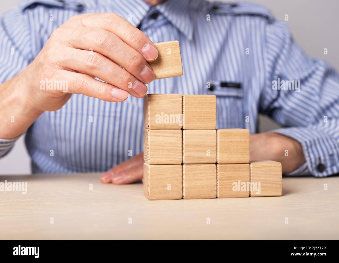 Uomo costruzione scala carriera da blocchi di legno. Sviluppo professionale e crescita personale. Promozione, successo e raggiungimento degli obiettivi nel lavoro. Foto di alta qualità Foto Stock