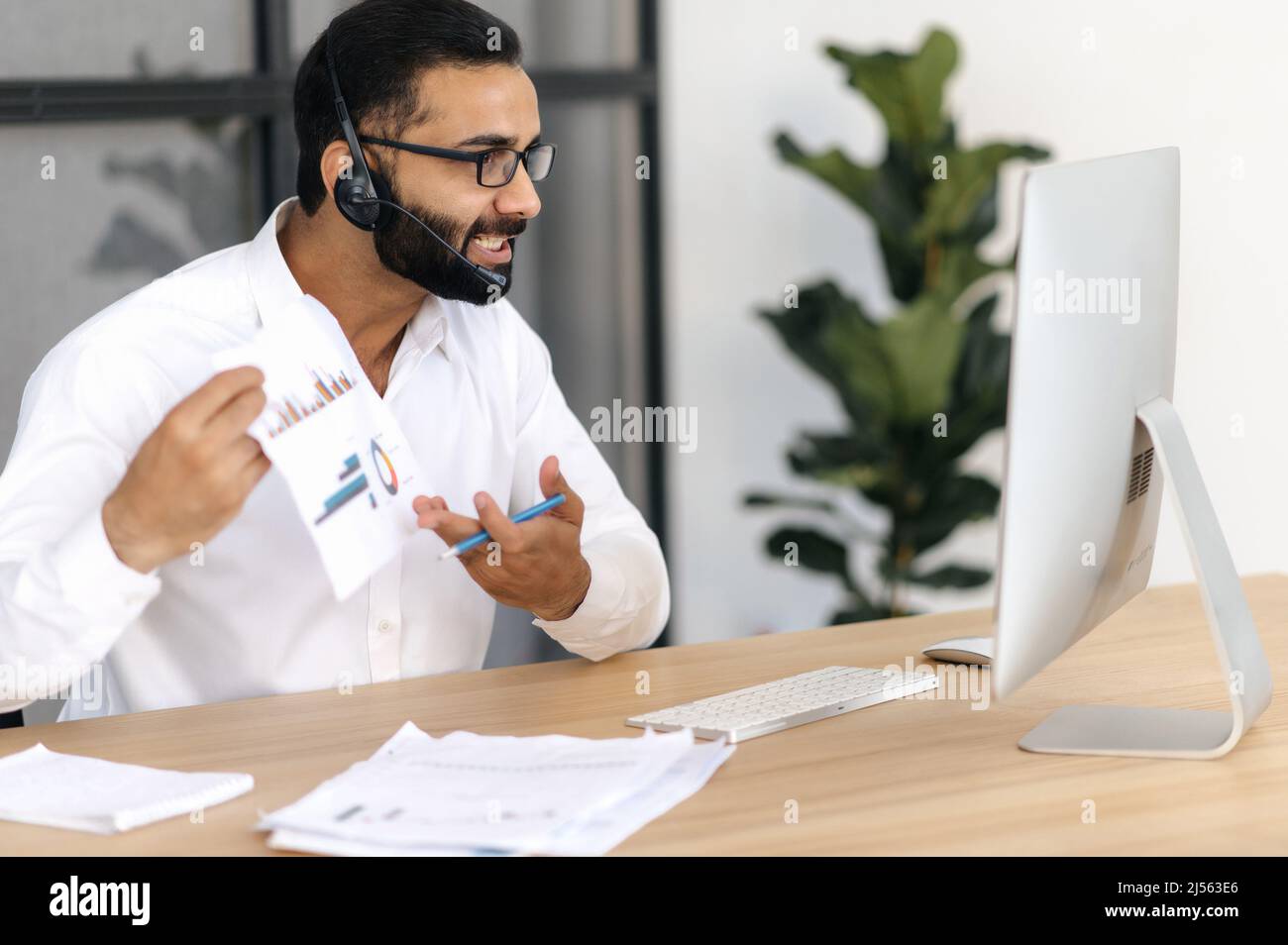 Irritato arrabbiato imprenditore indiano o arabo, influente uomo d'affari, parla tramite videochiamata con i partner, discute e analizza un business report, mostra un grafico per i suoi interlocutori, irritato Foto Stock