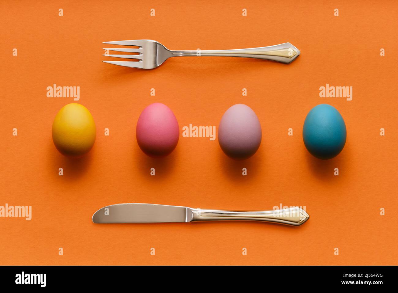 Sfondo pasquale astratto con uova colorate in fila con forchetta e coltello Foto Stock