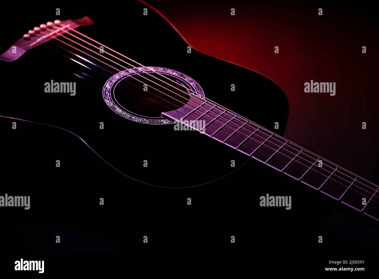 chitarra nera su sfondo scuro sotto fascio di luce rossa. musica chitarra basso concetto chiave Foto Stock