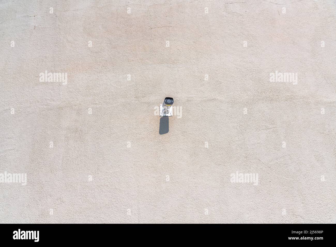 Lone telecamera di sicurezza su un muro a San Jose, California. Telecamera di sorveglianza montata a parete al centro di una parete di cemento sullo sfondo. Foto Stock
