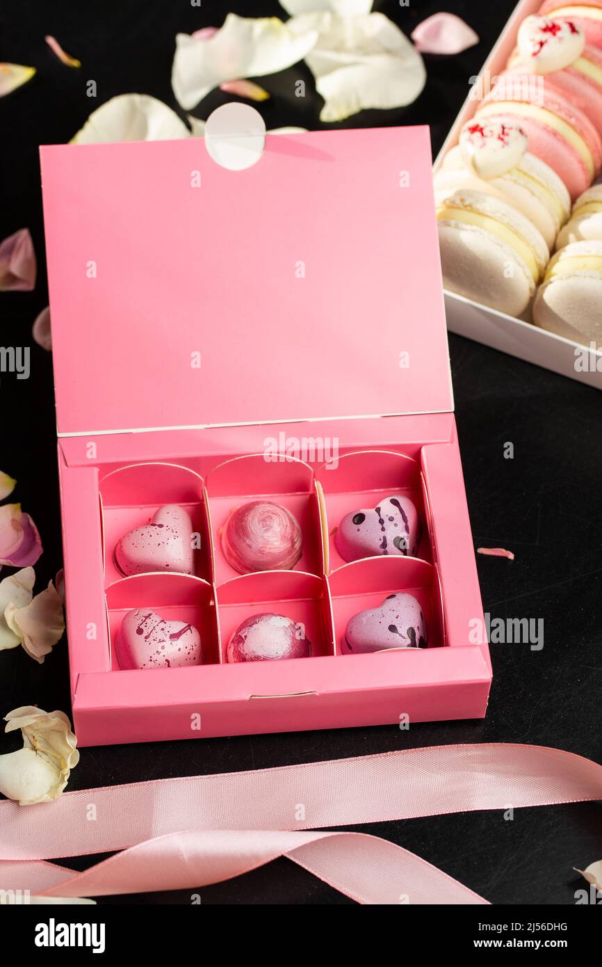 Caramelle di lusso al cioccolato rosa fatte a mano in scatola rosa isolata su sfondo scuro. Esclusivo bonbon artigianale. Concetto di pubblicità di prodotto per pasticceria Foto Stock