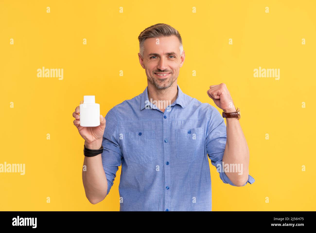 ragazzo felice che mostra la bottiglia di vitamina su sfondo giallo, supplemento Foto Stock