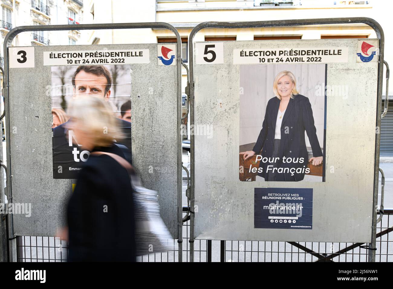 Parigi, Francia, 20 aprile 2022, Un pedone trasmette poster ufficiali della campagna su un cartellone elettorale (cartello). Poster presidenziali sui loro consigli elettorali. Illustrazione del 20 aprile 2022 a Parigi, Francia. Gli elettori francesi si dirigono ai sondaggi per votare il 24 aprile 2022 per il secondo turno delle elezioni presidenziali, per eleggere il loro nuovo presidente della Repubblica tra Emmanuel Macron e Marine le Pen. Foto Stock