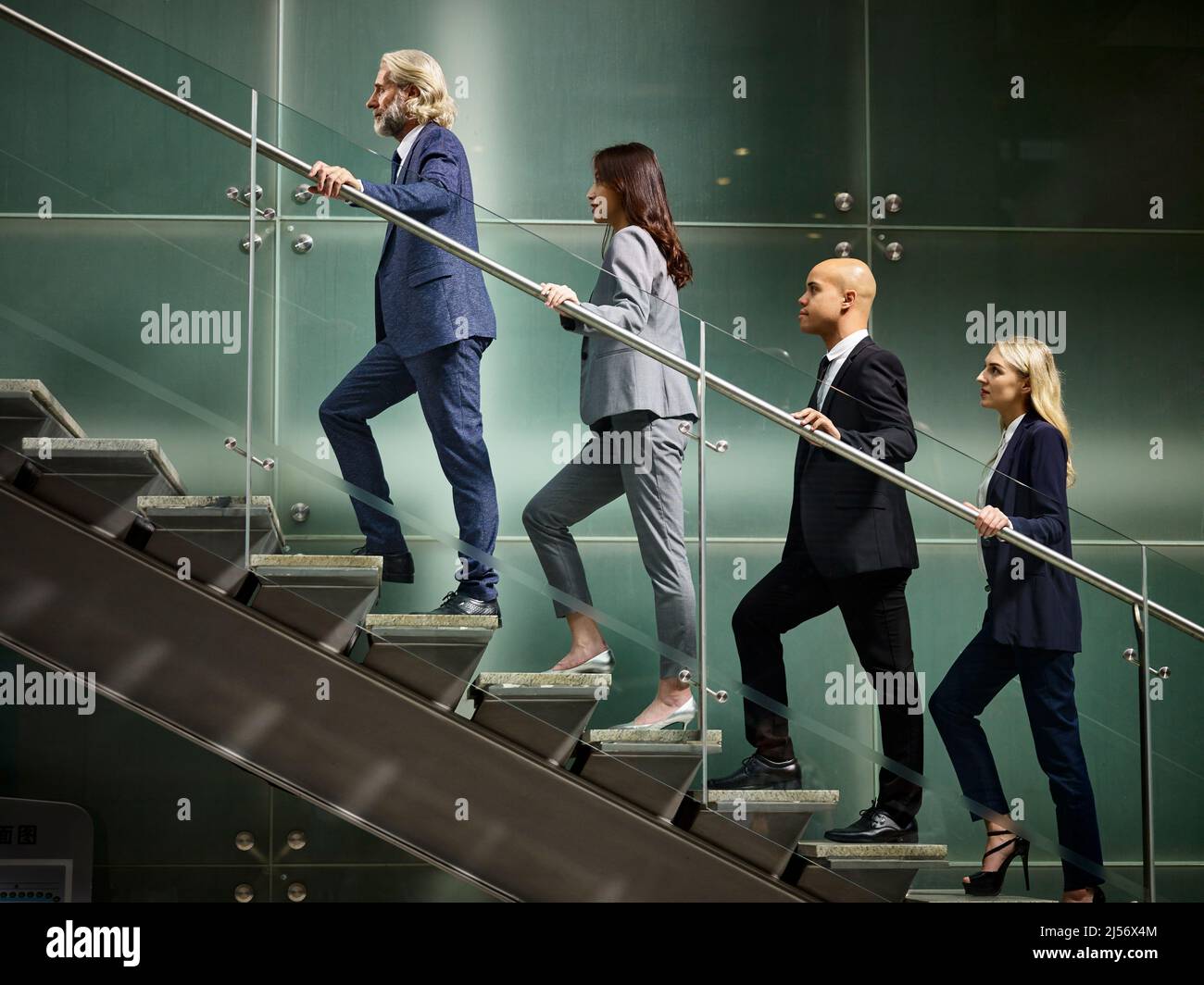 Multinazionale e multietnica corporate business persone maschio e femmina salendo le scale in una linea in un ufficio moderno edificio. Foto Stock