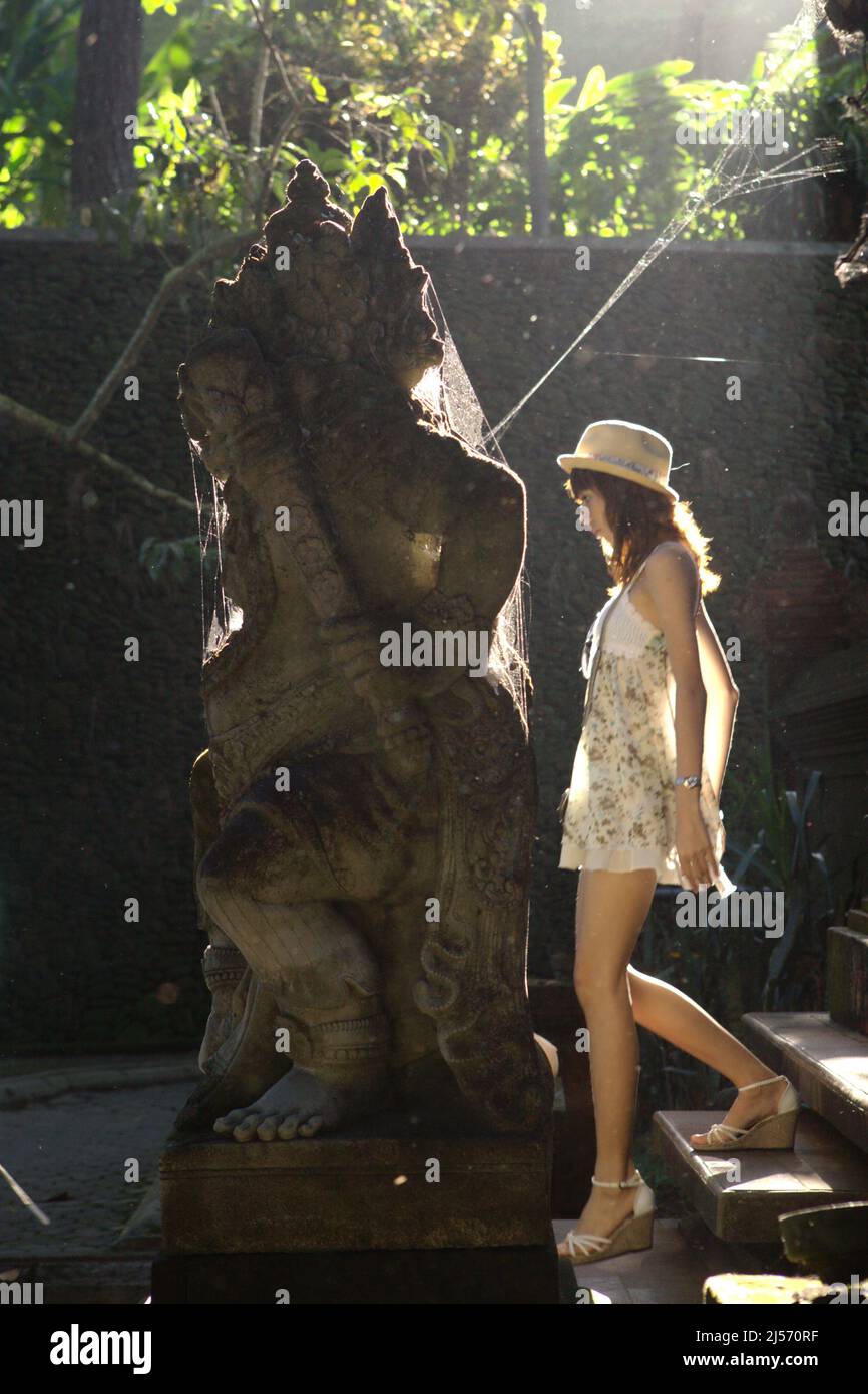 Una donna turistica che cammina dietro una statua dvarapala nel complesso del tempio Tirta Empul a Tampaksiring, Gianyar, Bali, Indonesia. Secondo Trip Advisor, Bali è stata la quarta destinazione più popolare al mondo nel periodo pre-Covid. L'ufficio di statistica della provincia di Bali ha menzionato che 6.275.210 turisti hanno visitato Bali nel 2019, il suo record più alto. Tuttavia, solo 1.069.473 hanno visitato l'Isola degli dei nel 2020 a causa della pandemia, seguita da solo 51 (calo del 100%) nel 2021. Foto Stock