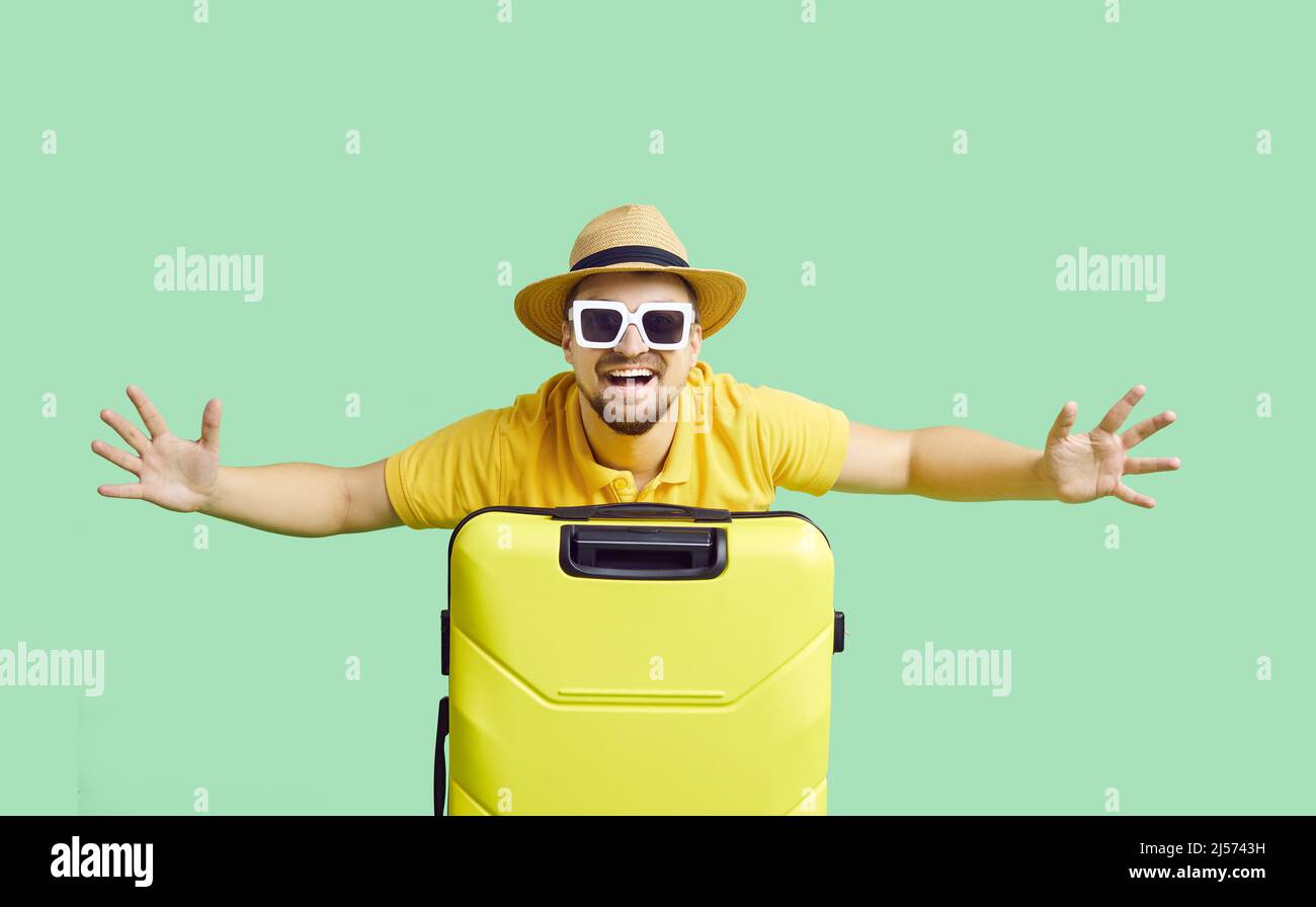 Uomo gioiosamente eccitato con valigia gialla su sfondo verde chiaro pronto per le vacanze estive. Foto Stock