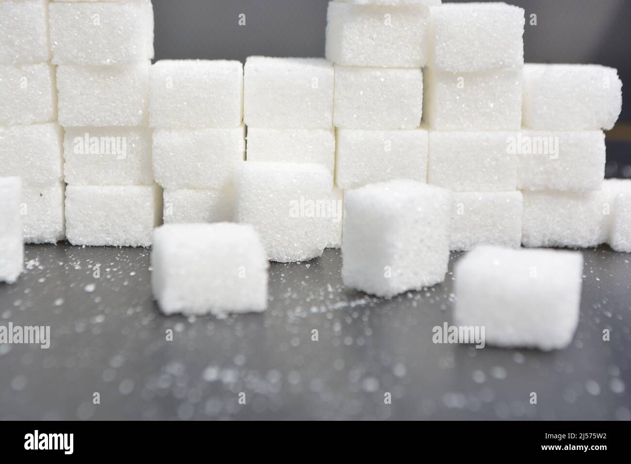 Passi fatti da cubetti di zucchero. Mucchio di cubetti di zucchero su una superficie grigia lucida, piramide di zucchero. Foto Stock